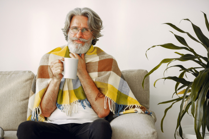 Older man wrapped in a blanket, holding a mug and sitting calmly—suggesting relief after tenant troubles