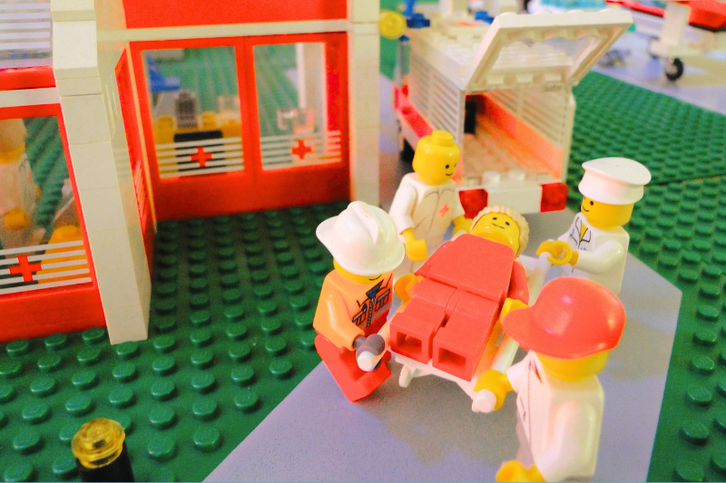 Lego tradie being carried on a stretcher by paramedics outside a hospital